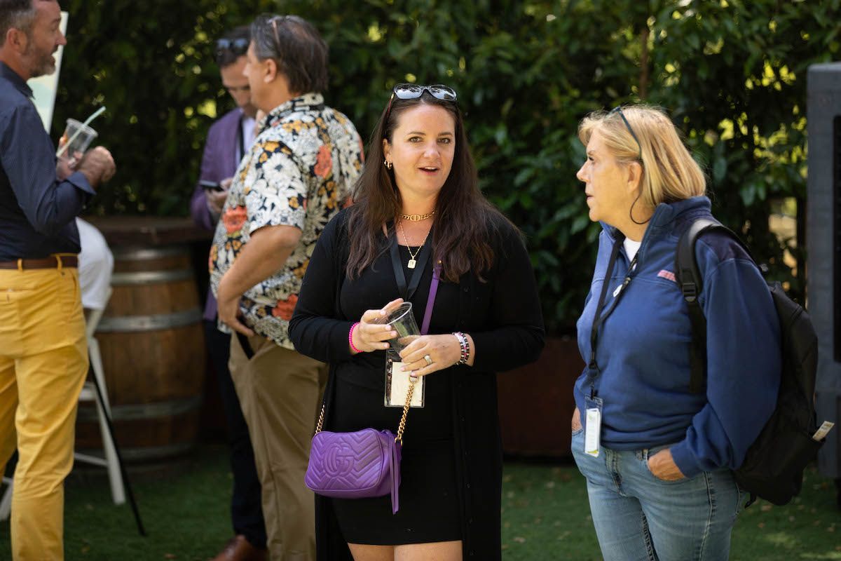 A group of people are standing on a lush green field talking to each other.