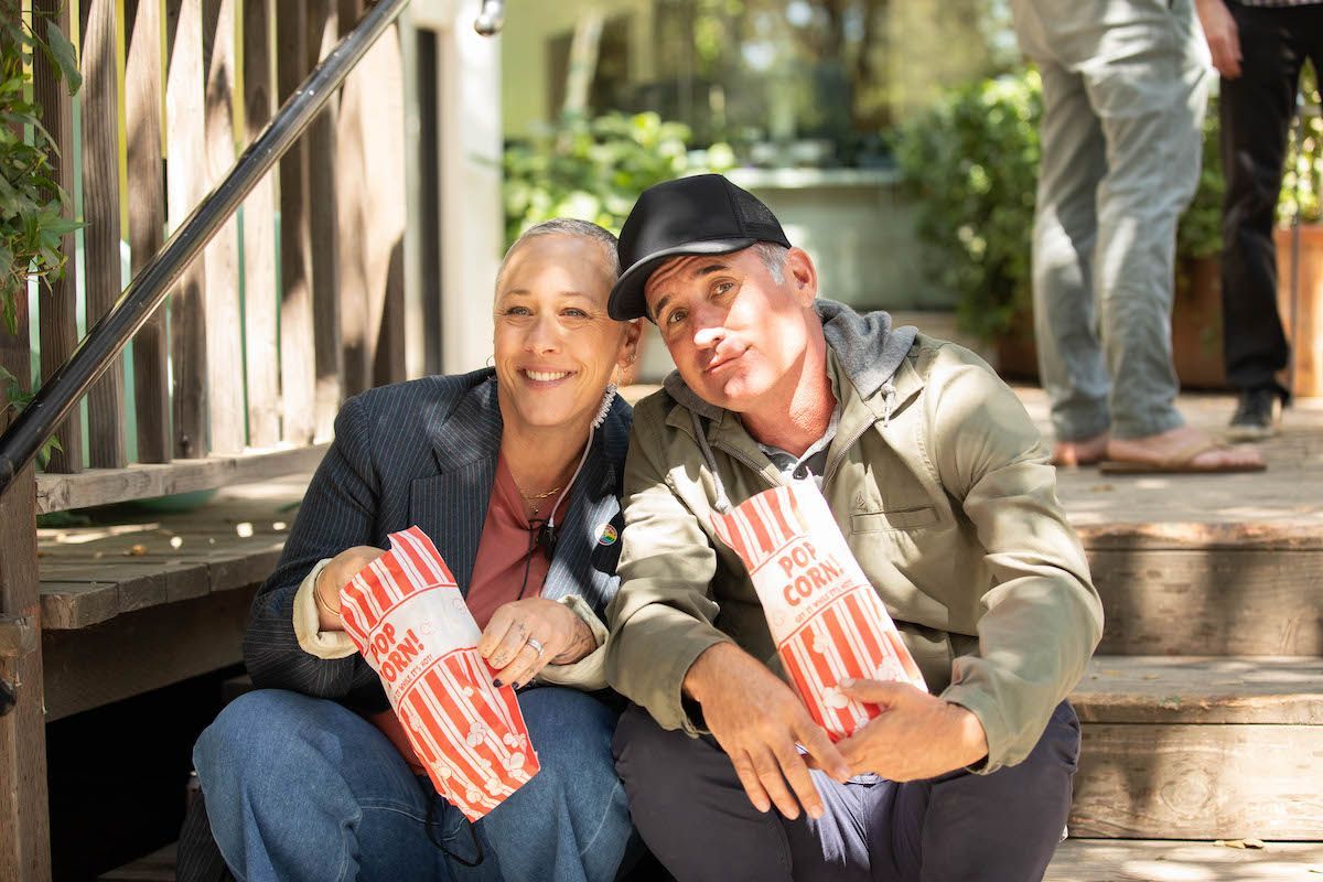 A man and a woman are sitting on a porch holding bags of popcorn.