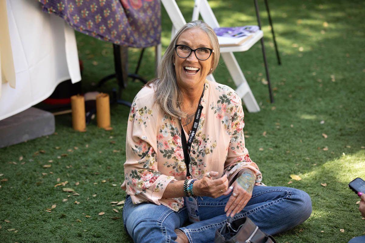 A woman is sitting on the grass with her legs crossed and smiling.