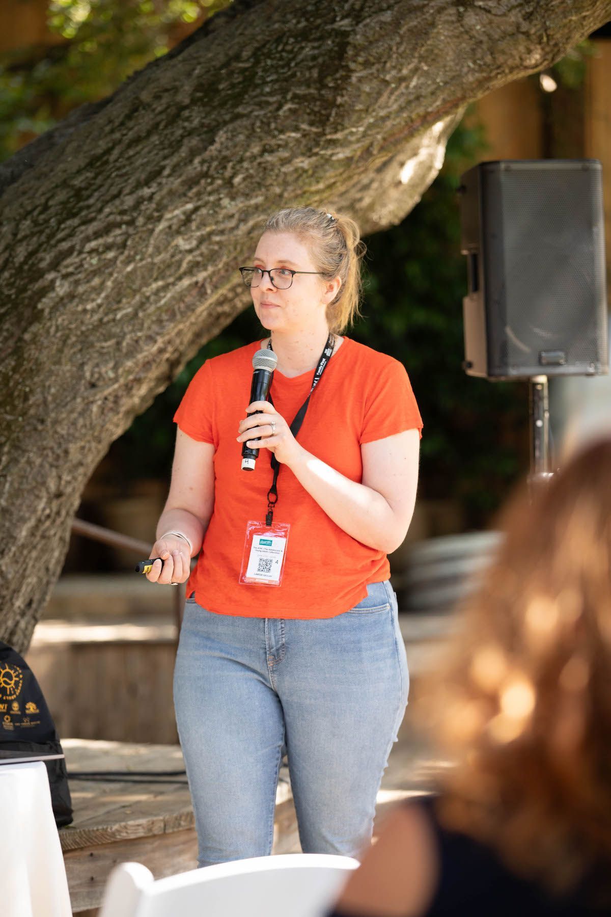 A woman is standing in front of a tree holding a microphone.