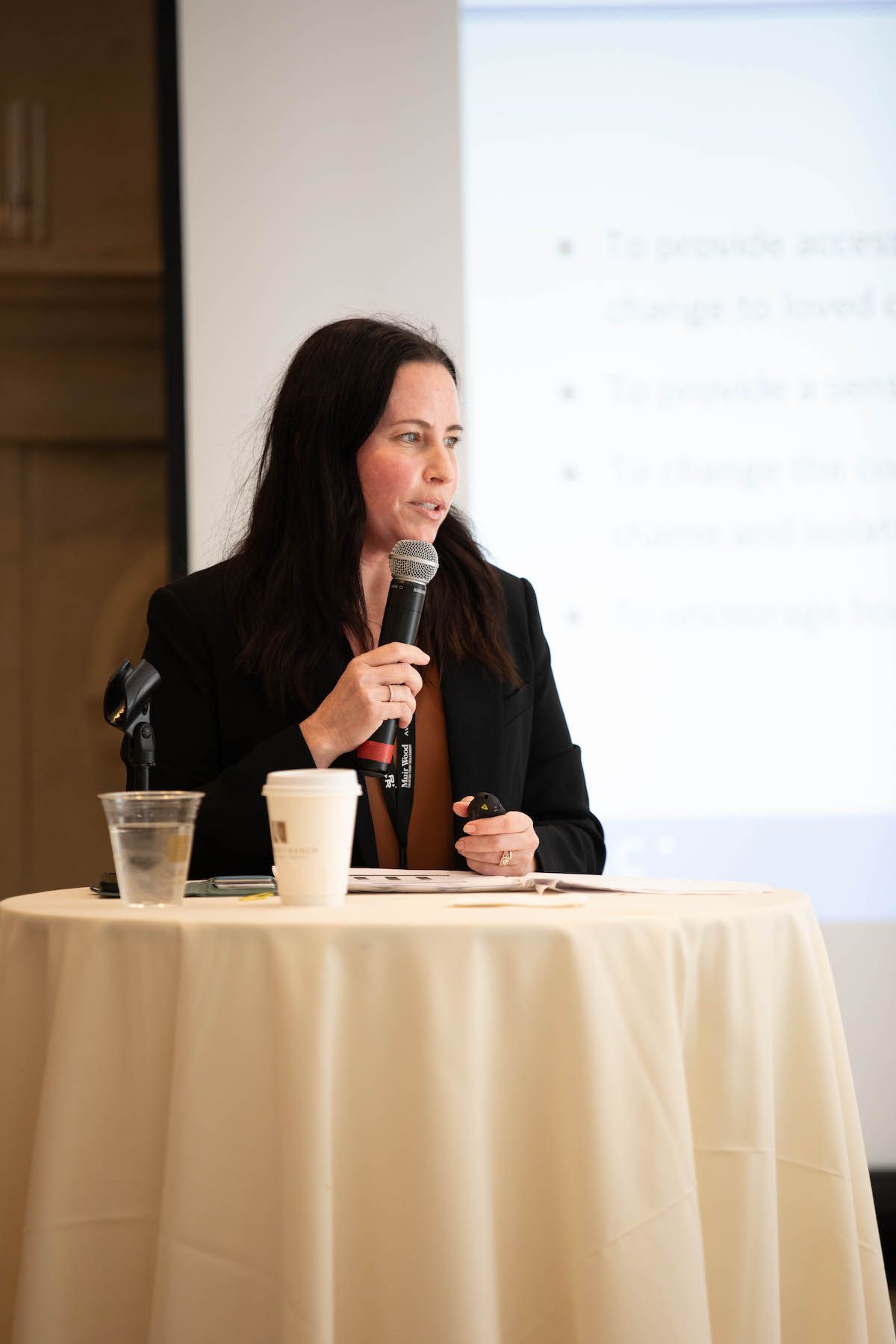 A woman is sitting at a table holding a microphone.
