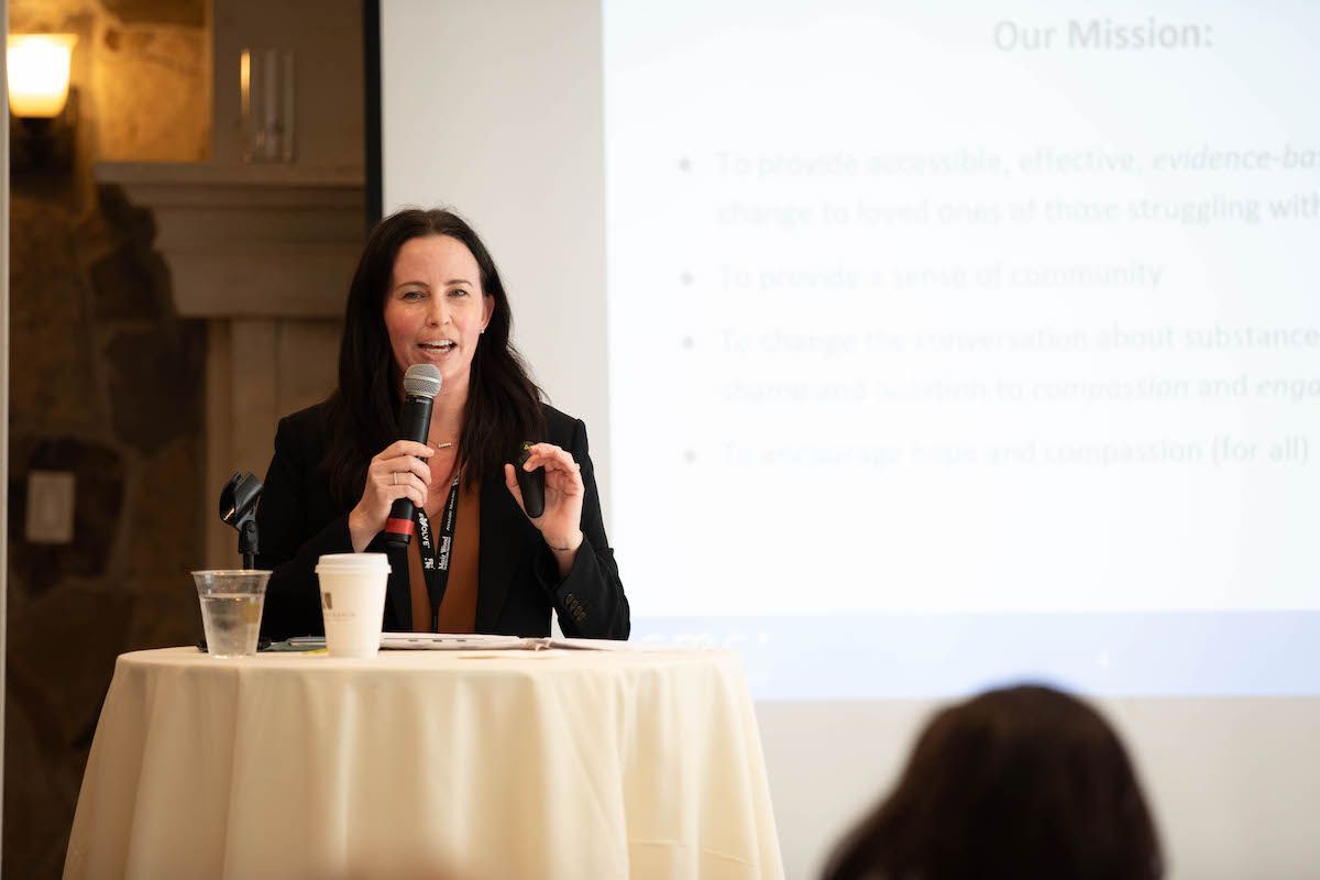 A woman is sitting at a table holding a microphone.