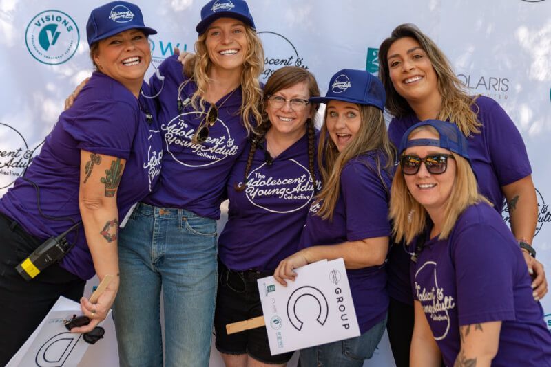 A group of women wearing purple shirts and blue hats are posing for a picture.