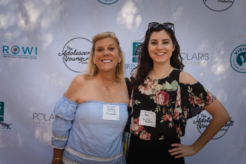 Two women are posing for a picture in front of a backdrop that says rowi