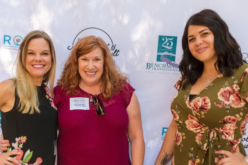 Four women are posing for a picture in front of a white wall.