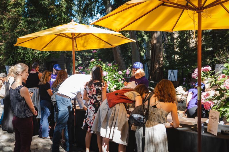 A group of people are standing under yellow umbrellas at a market.
