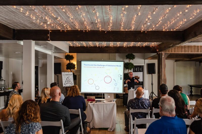 A group of people are sitting in chairs in front of a projector screen.