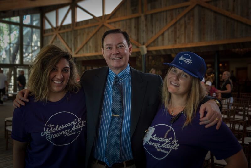 A man in a suit and tie is posing for a picture with two women wearing purple shirts.