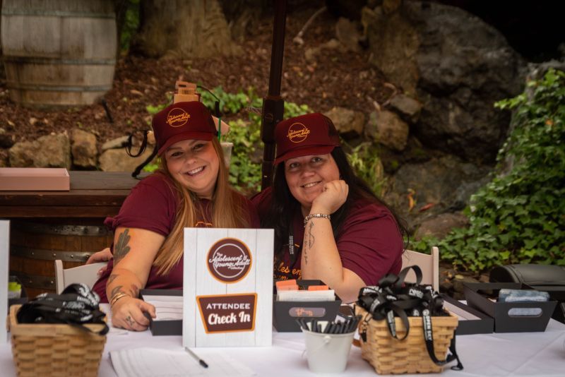Two women are sitting at a table with a sign that says check in.