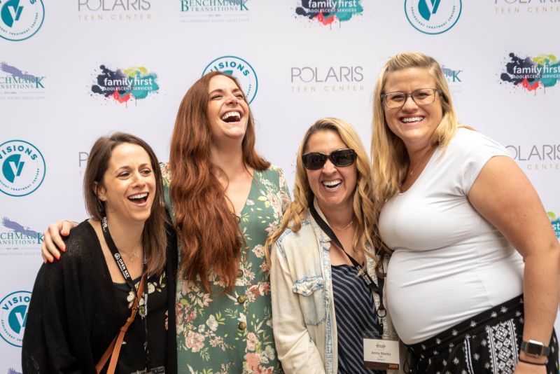 A group of women are posing for a picture in front of a wall.