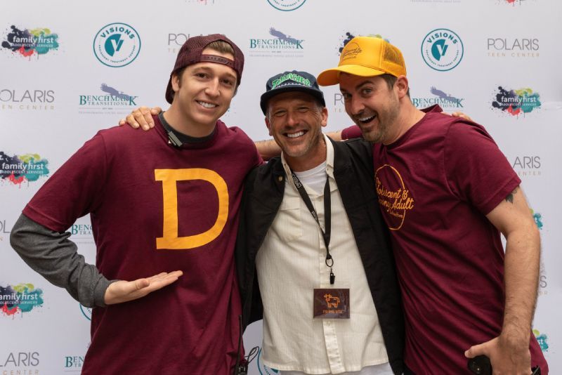 Three men are posing for a picture and one of them is wearing a shirt with the letter d on it.