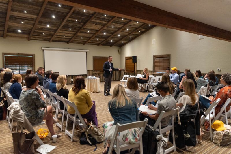 A man is giving a presentation to a group of people sitting in chairs in a large room.