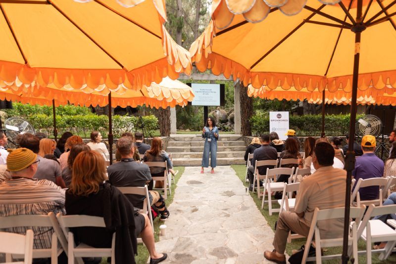 A woman is giving a presentation to a group of people under umbrellas.