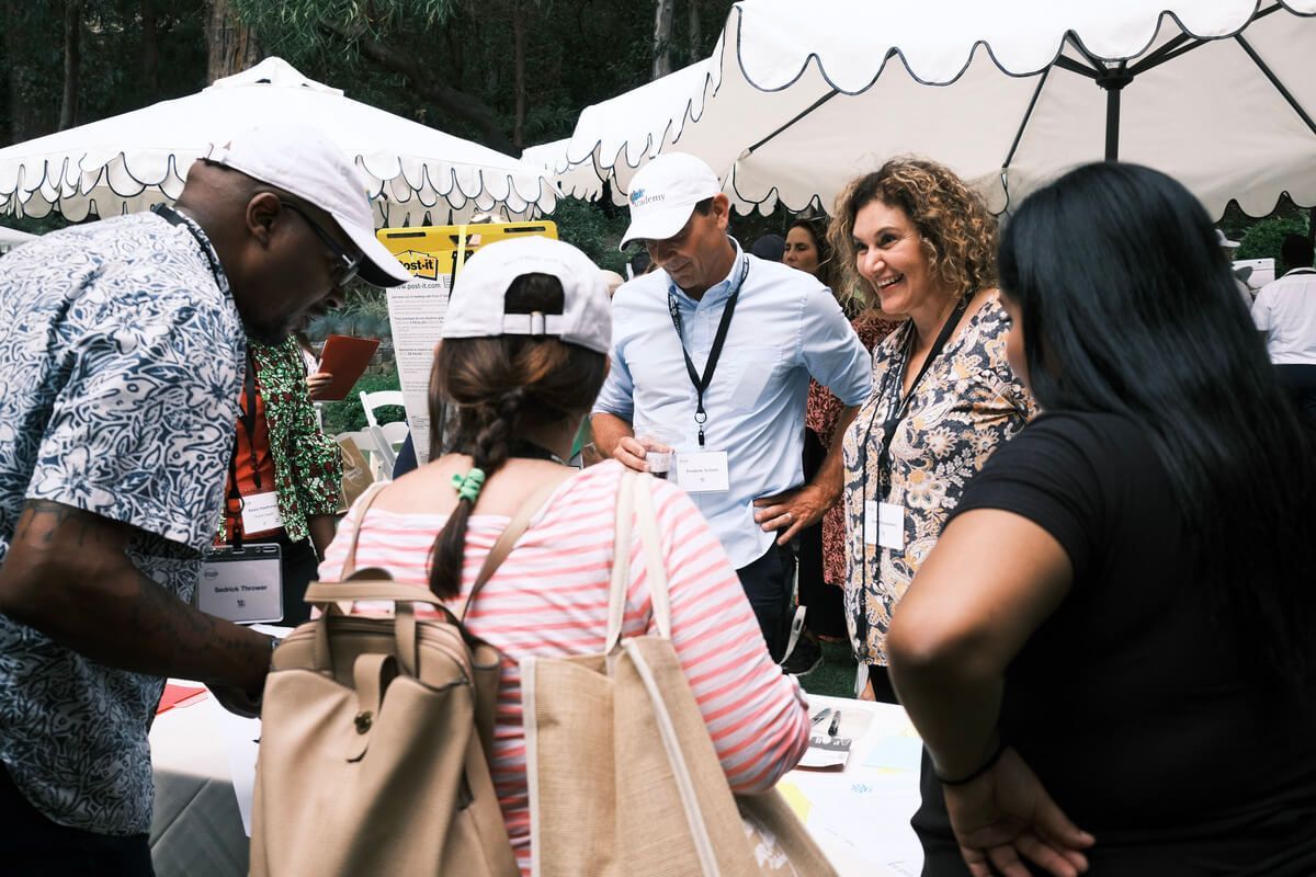 A group of people are standing around a table under an umbrella.
