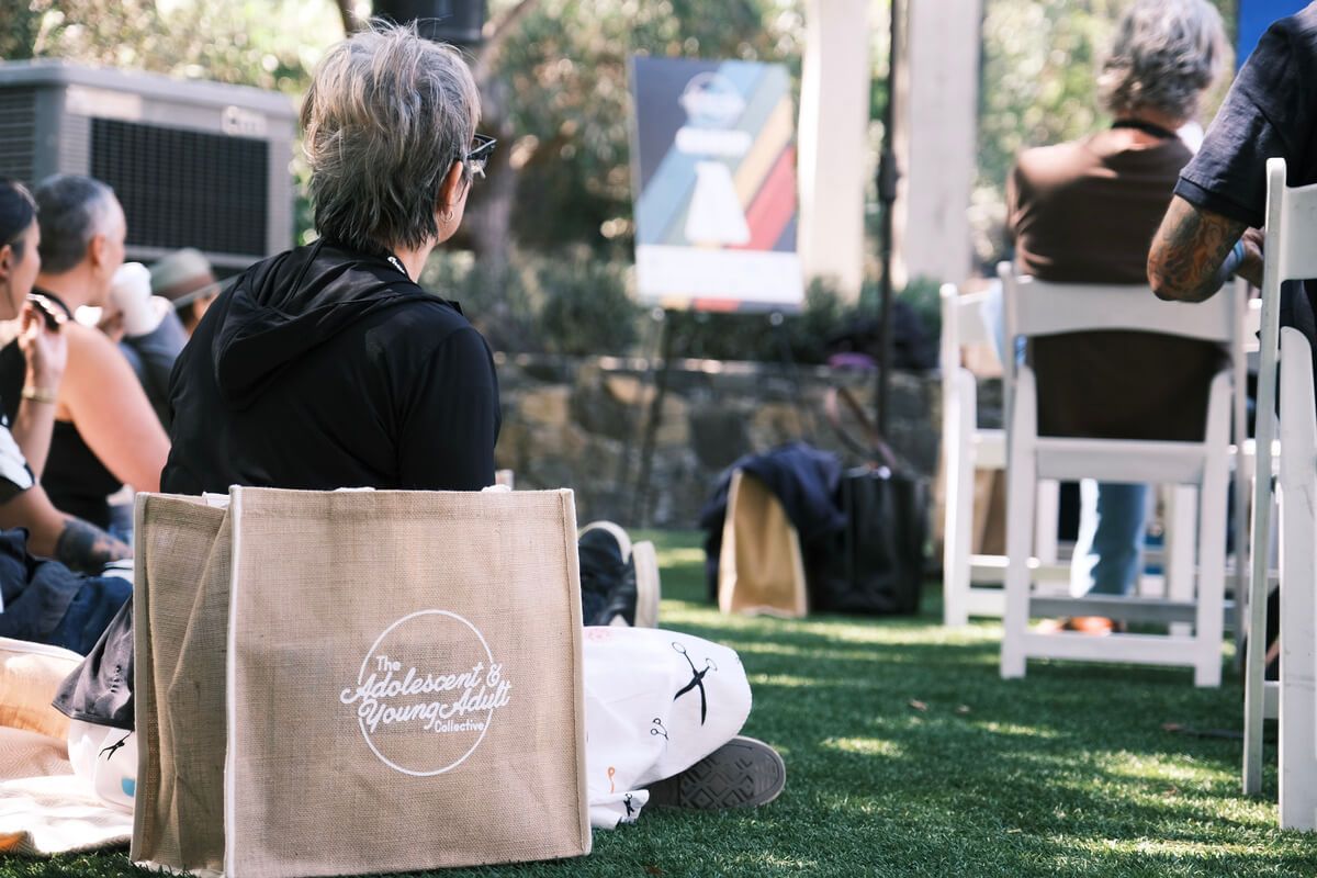 A woman is sitting on the grass with a bag in front of her.
