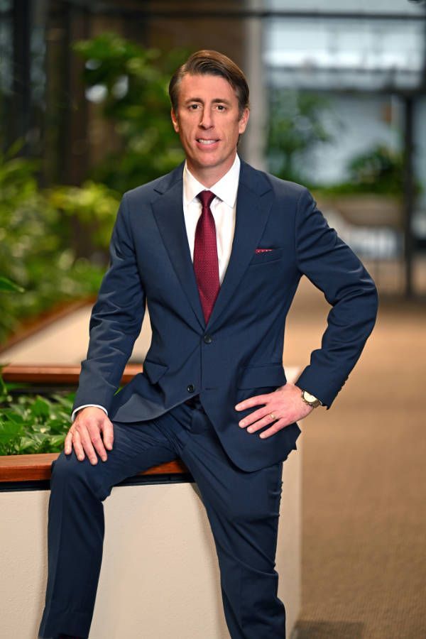 Woman with short brown hair, smiling in a green jacket, outdoor background.