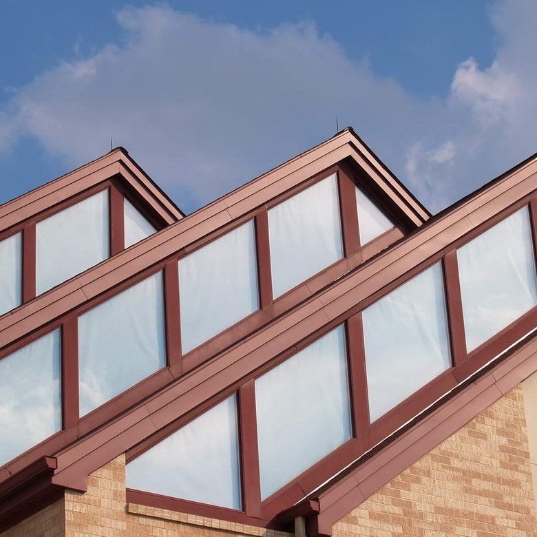 Angled skylights with brown frames on a brick building against a blue sky