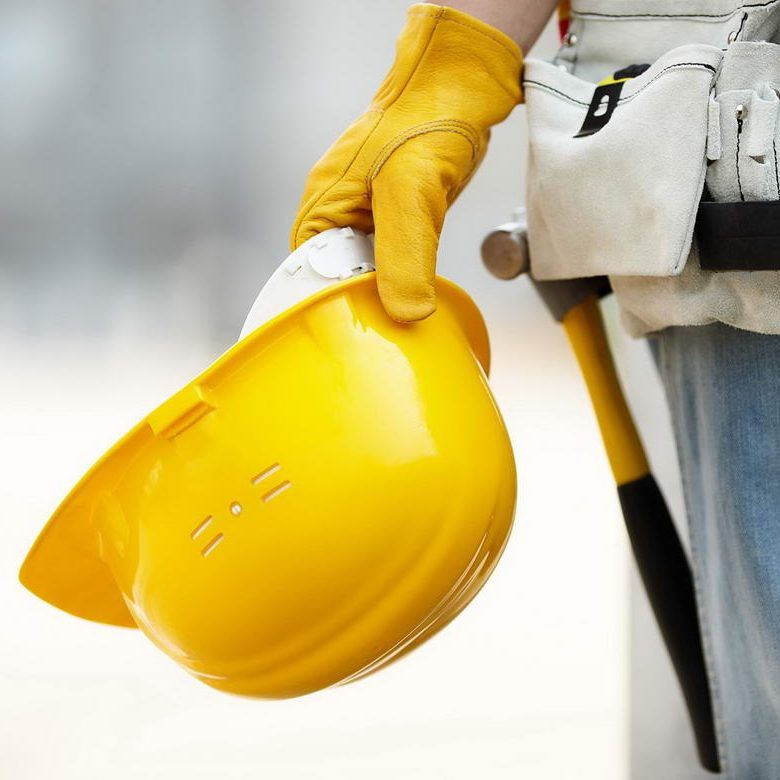 Worker holding a yellow hard hat and white tool belt at a construction site