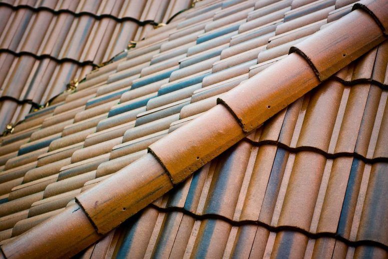 Close-up of a terracotta tiled roof with diagonal ridge tiles and weathered brown, tan, and blue-gray shingles
