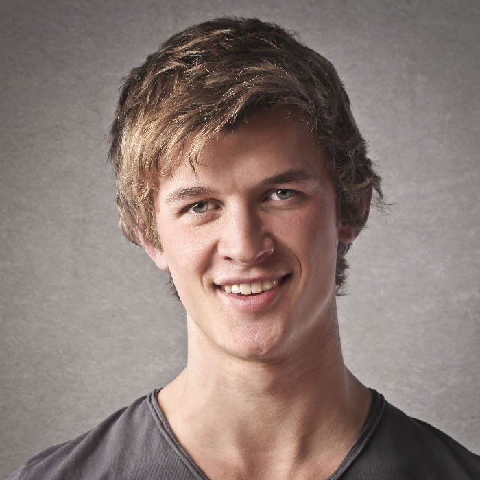 Smiling person with short blond hair against a gray background
