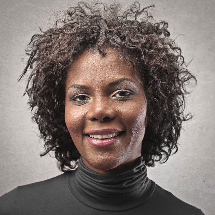 Portrait of a smiling person with curly hair in a dark turtleneck against a gray background