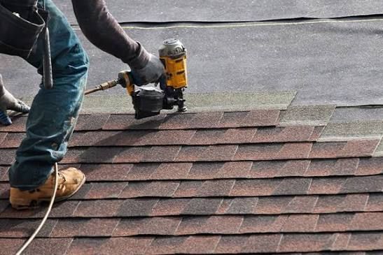 Worker nailing asphalt shingles onto a roof during repair work