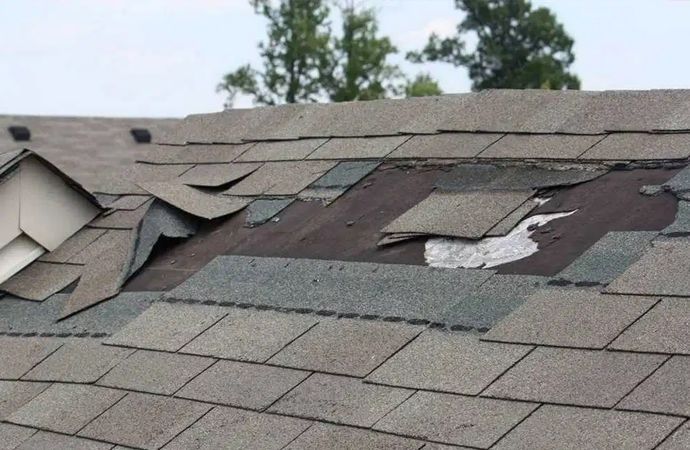 Damaged shingle roof with torn sections and exposed underlayment near the ridge