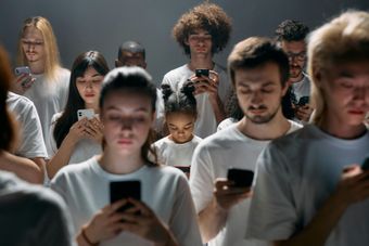 Um grande grupo de pessoas está em uma fila olhando para seus celulares.