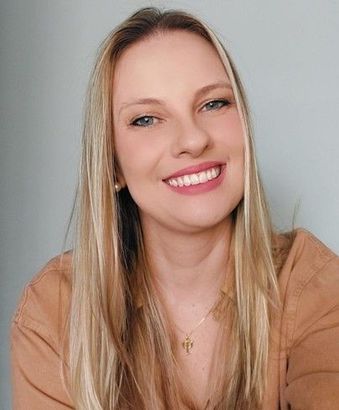 Uma mulher vestindo um suéter marrom e um colar está sorrindo para a câmera.