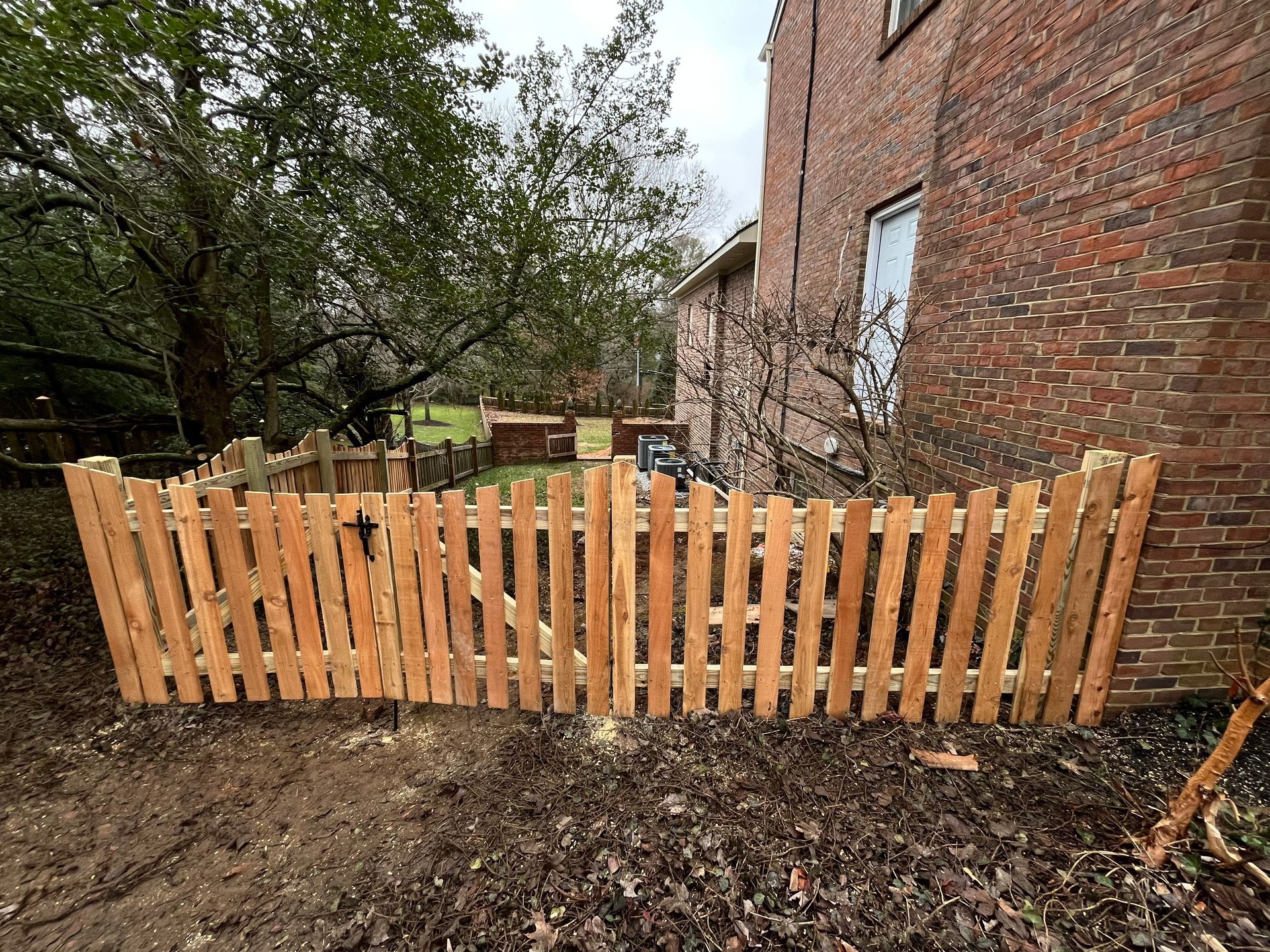 A wooden picket fence is sitting in front of a brick building.