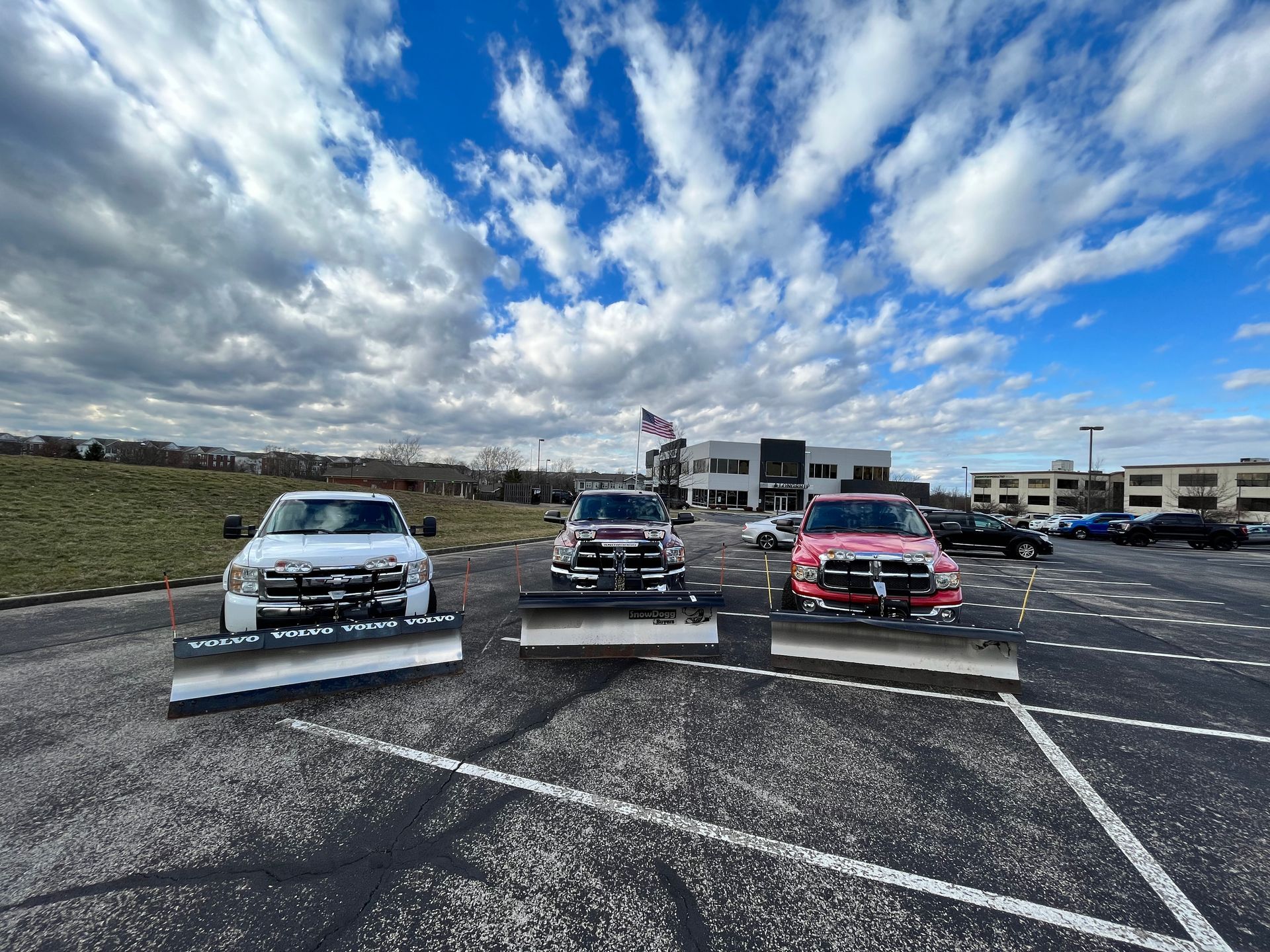 Three snow plows are parked in a parking lot.