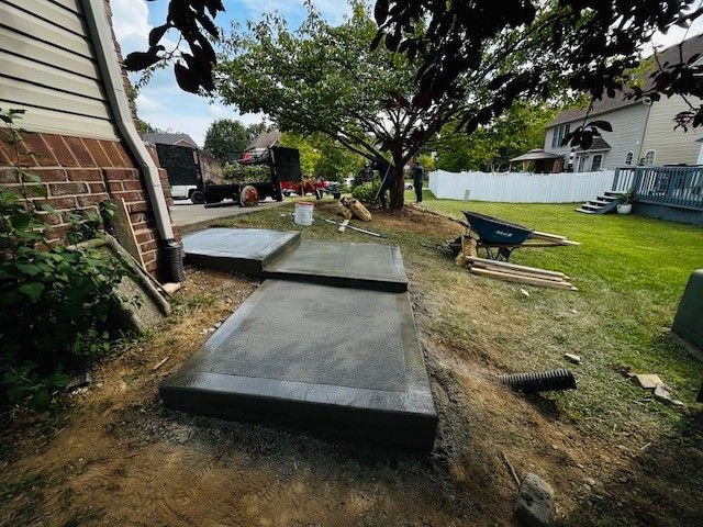 A concrete walkway is being built in the backyard of a house.