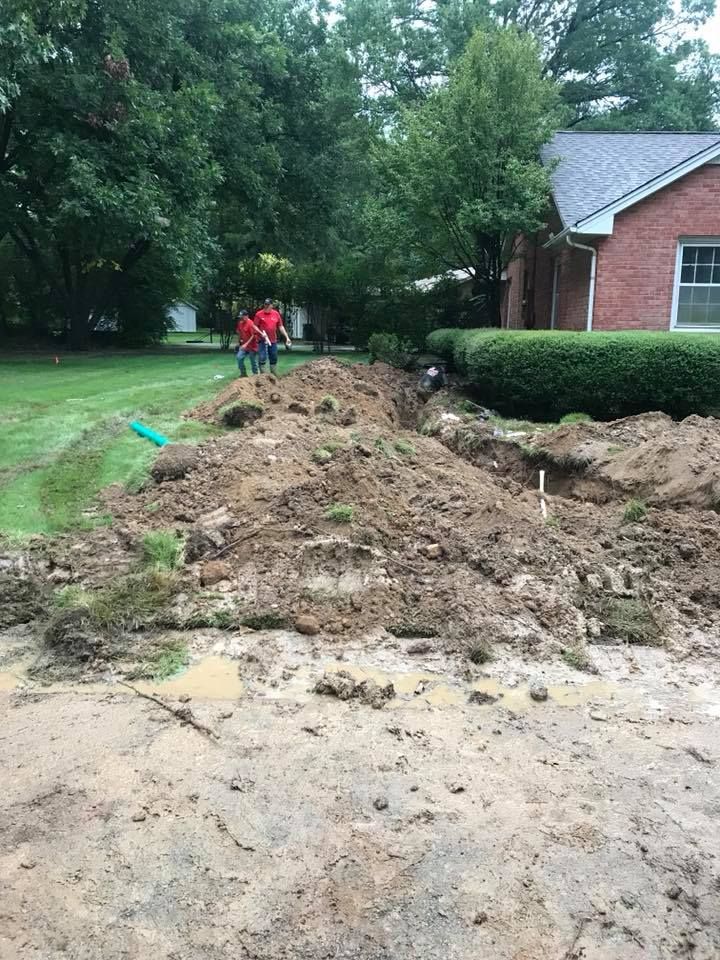 A Trench Dug in Muddy Ground Next to a House and Lawn