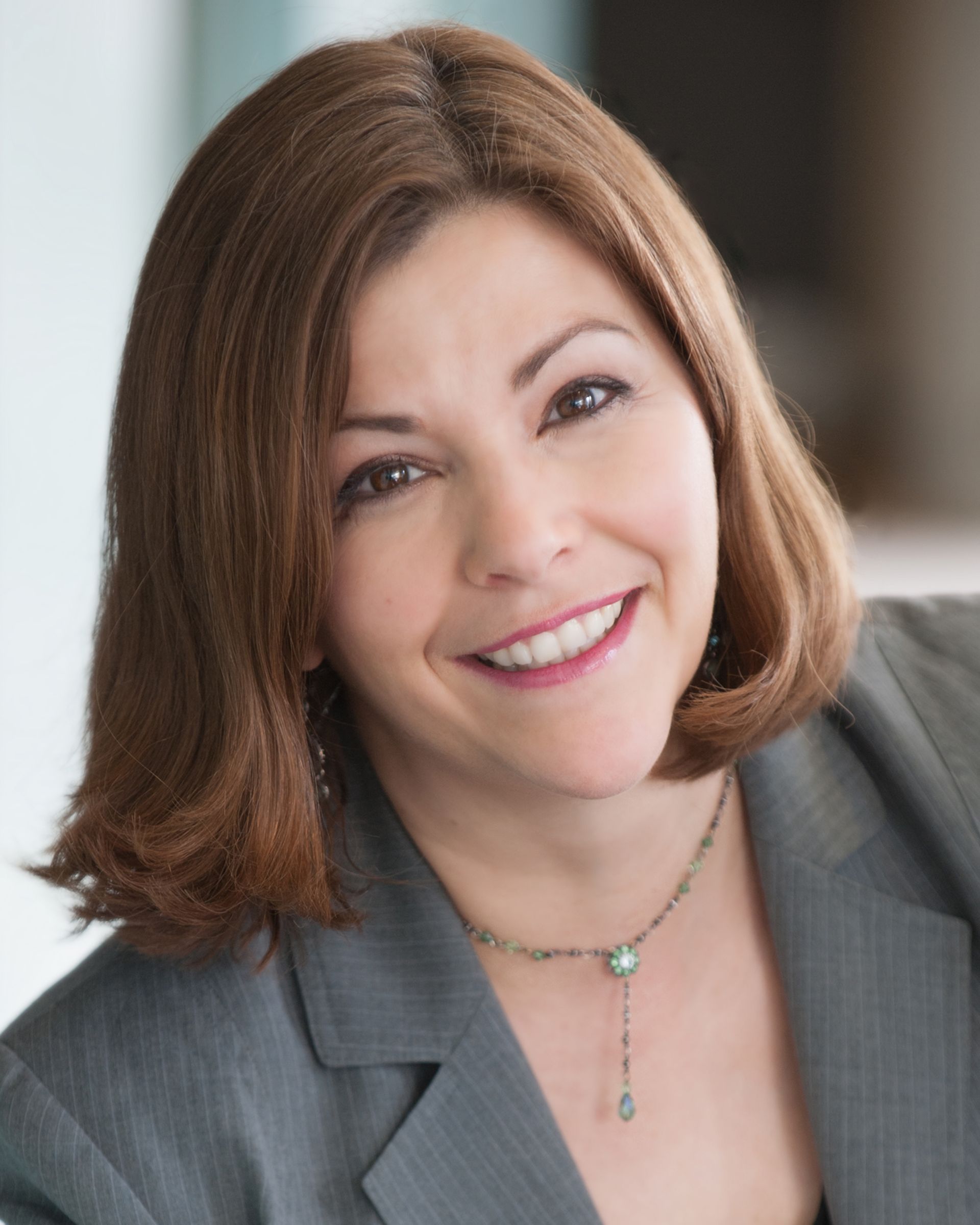 A woman in a suit and necklace smiles for the camera