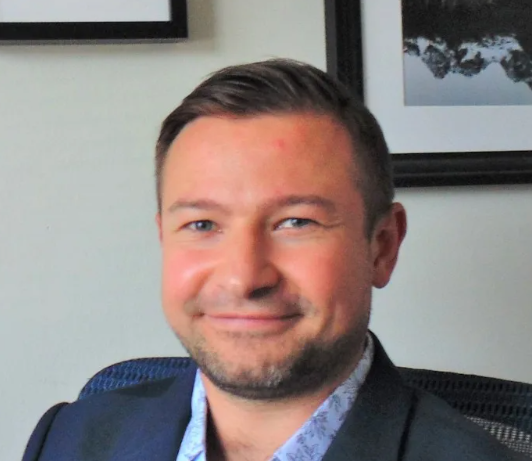 A man in a suit is smiling in front of a framed picture