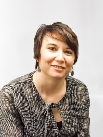 A woman with short hair and earrings is smiling for the camera