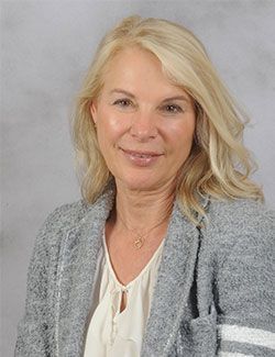 A woman wearing a gray jacket and a white shirt is smiling for the camera.