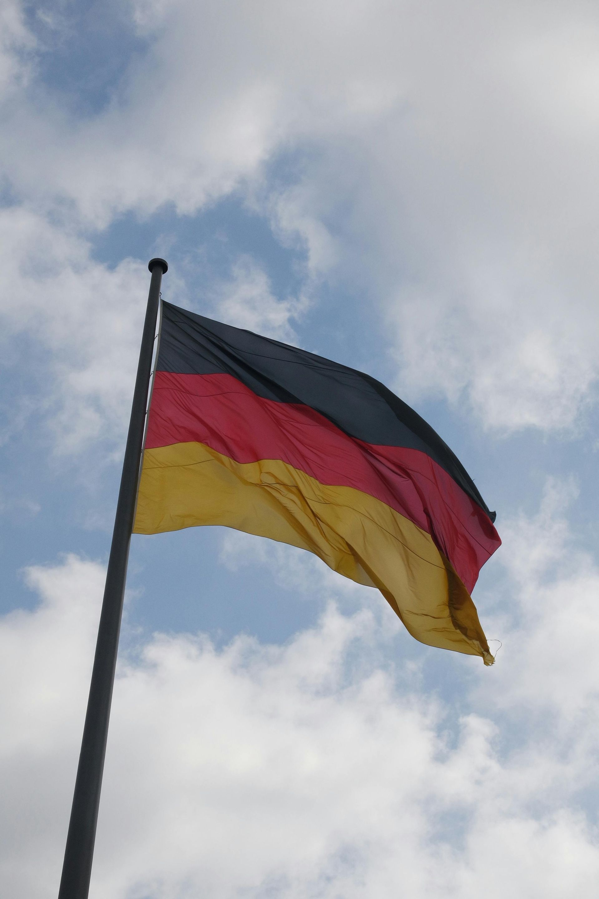 A german flag is waving in the wind against a cloudy blue sky