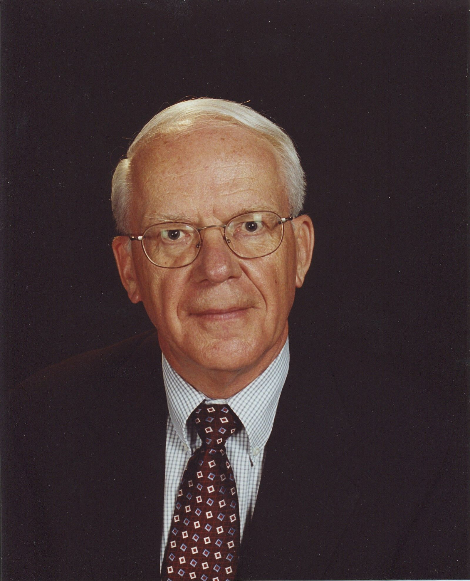 A man wearing glasses and a tie looks at the camera