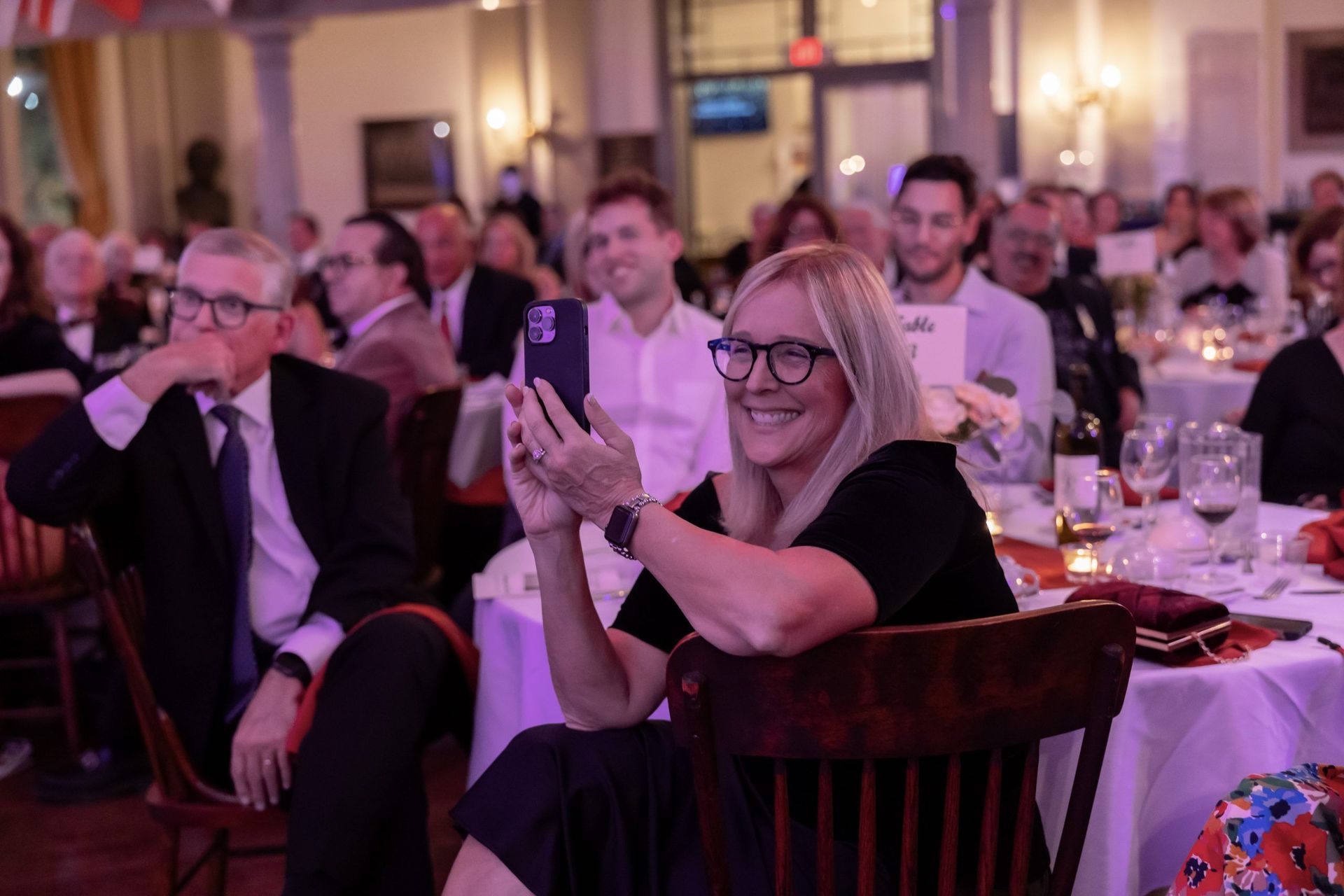 A woman is sitting in a chair taking a picture of herself with her phone.