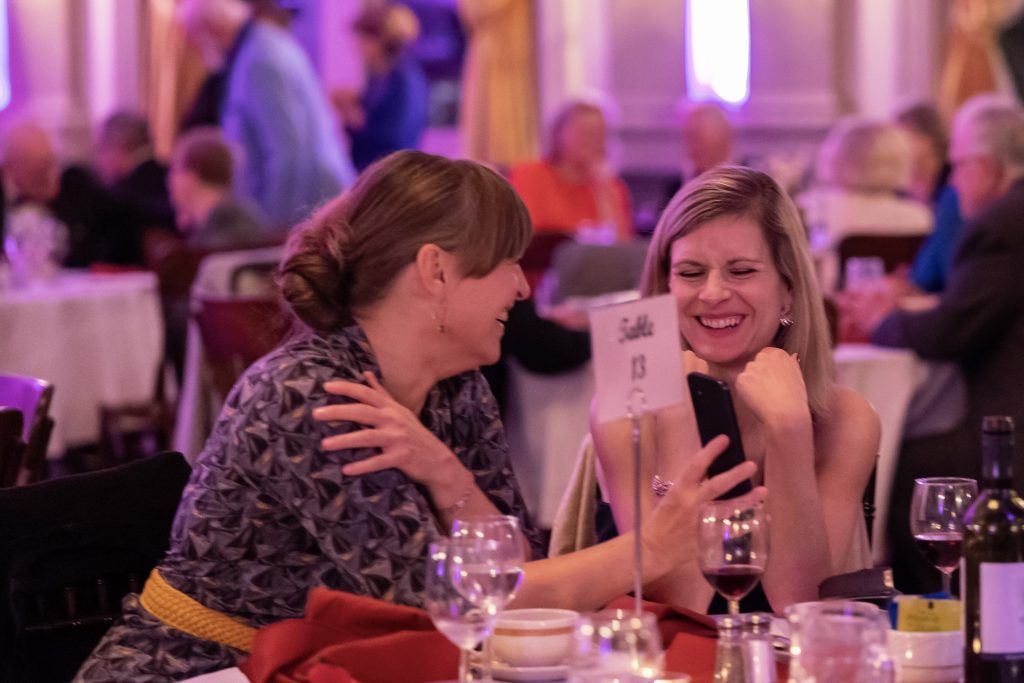 Two women are sitting at a table looking at a cell phone.