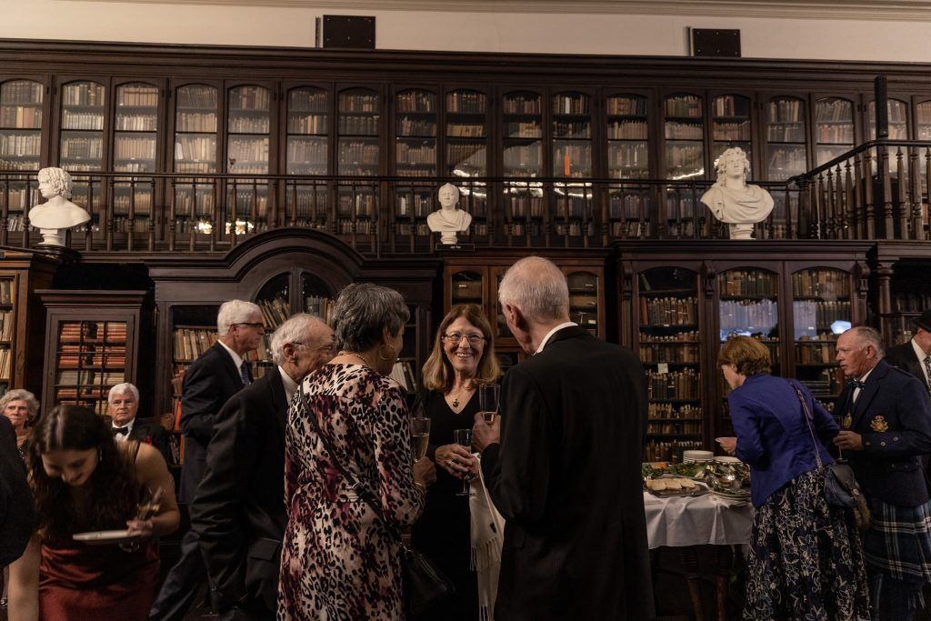 A group of people are standing in a library talking to each other.