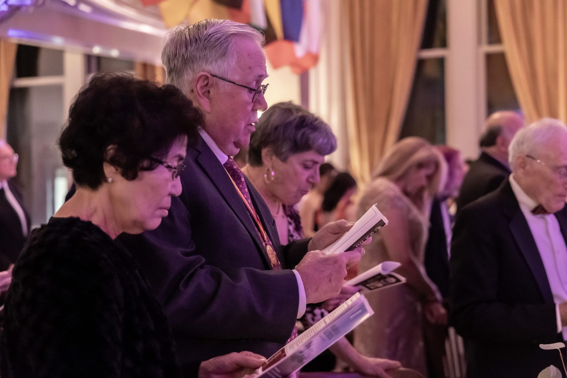 A group of people are standing in a room reading books.