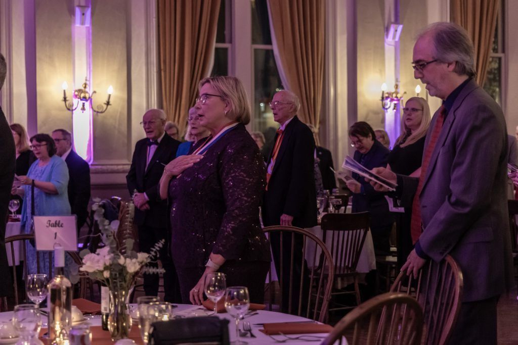A group of people are standing in a room with tables and chairs.