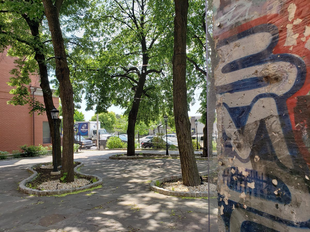 A brick wall with graffiti on it and trees in the background.