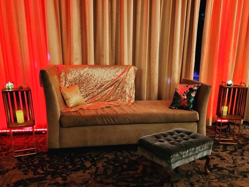 A cozy lounge area with a chaise lounge, ottoman, and side tables lit by red and orange ambient light.