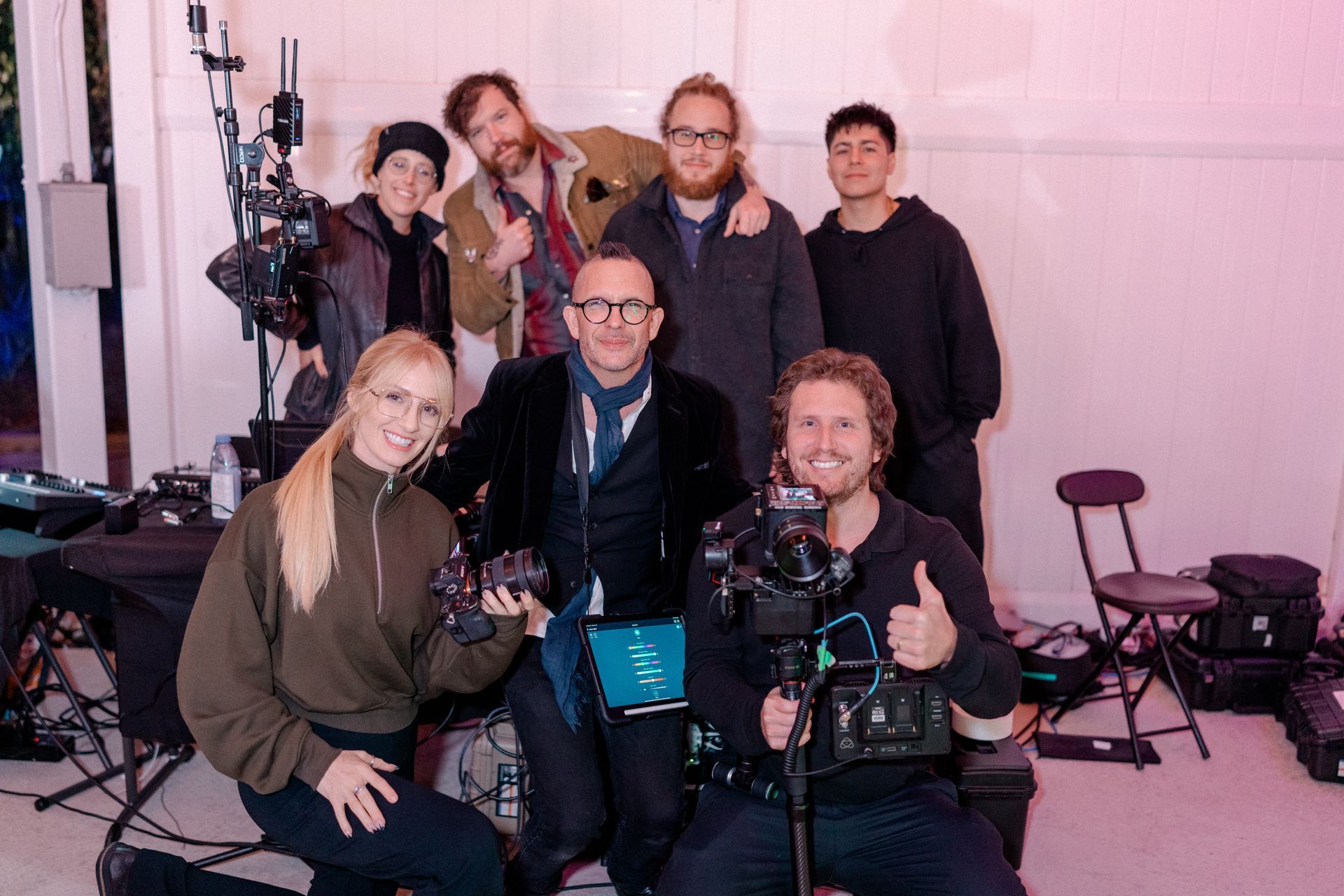 Film crew poses for a group photo.  Smiling people with cameras and equipment in a studio setting.