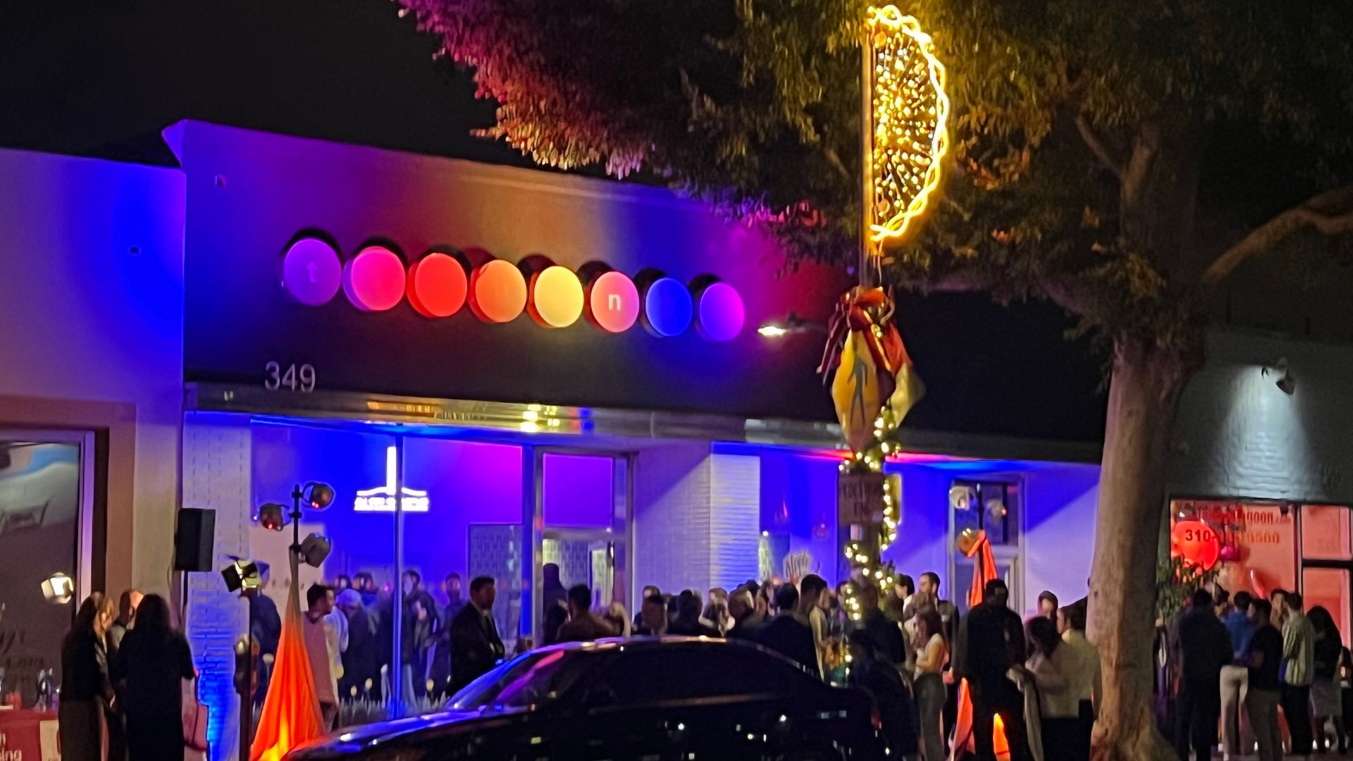 Night exterior of a building lit with purple and rainbow lights, people gathered outside.