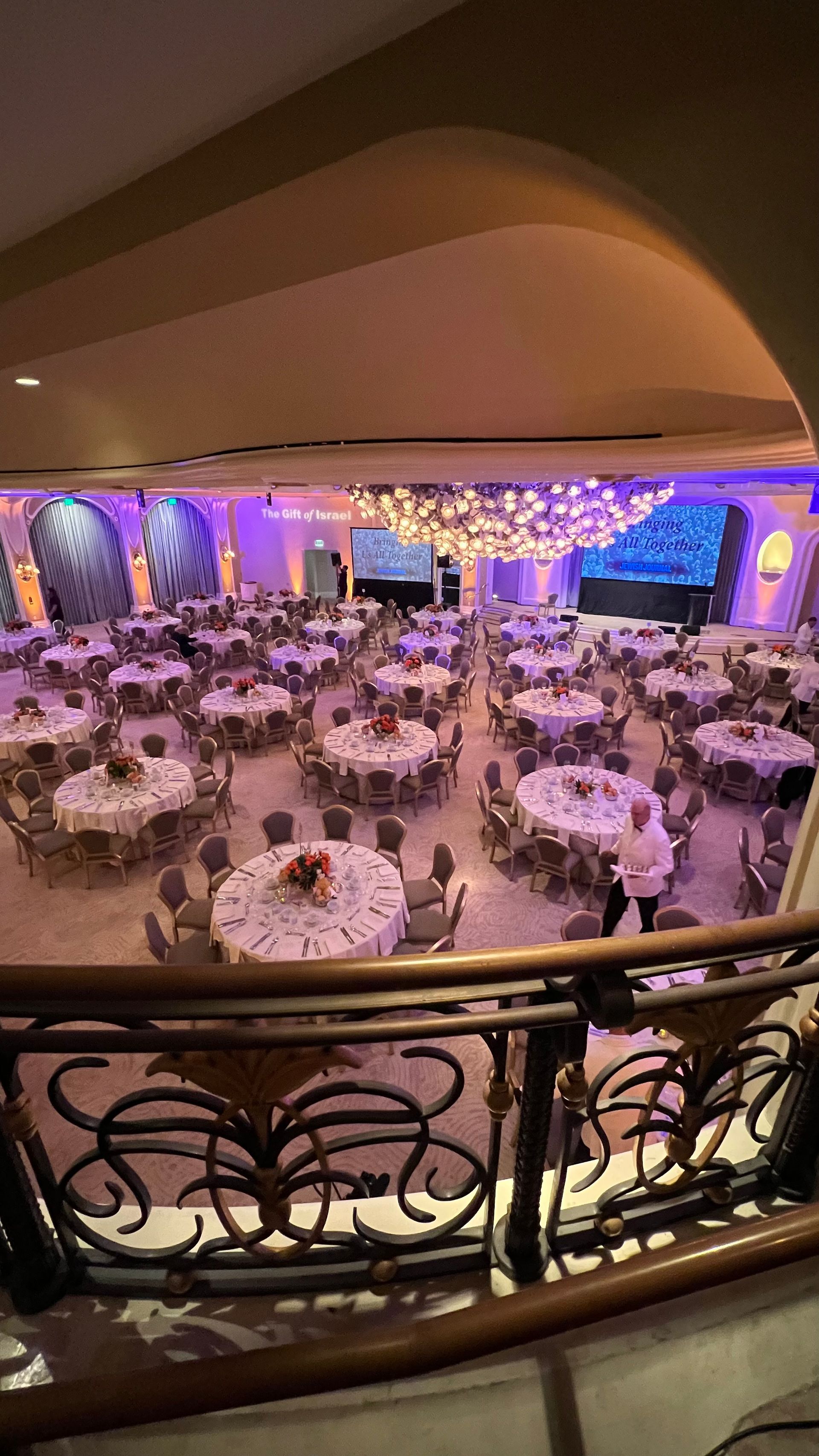 Large ballroom with round tables set for a formal event, decorated with flowers and soft lighting.