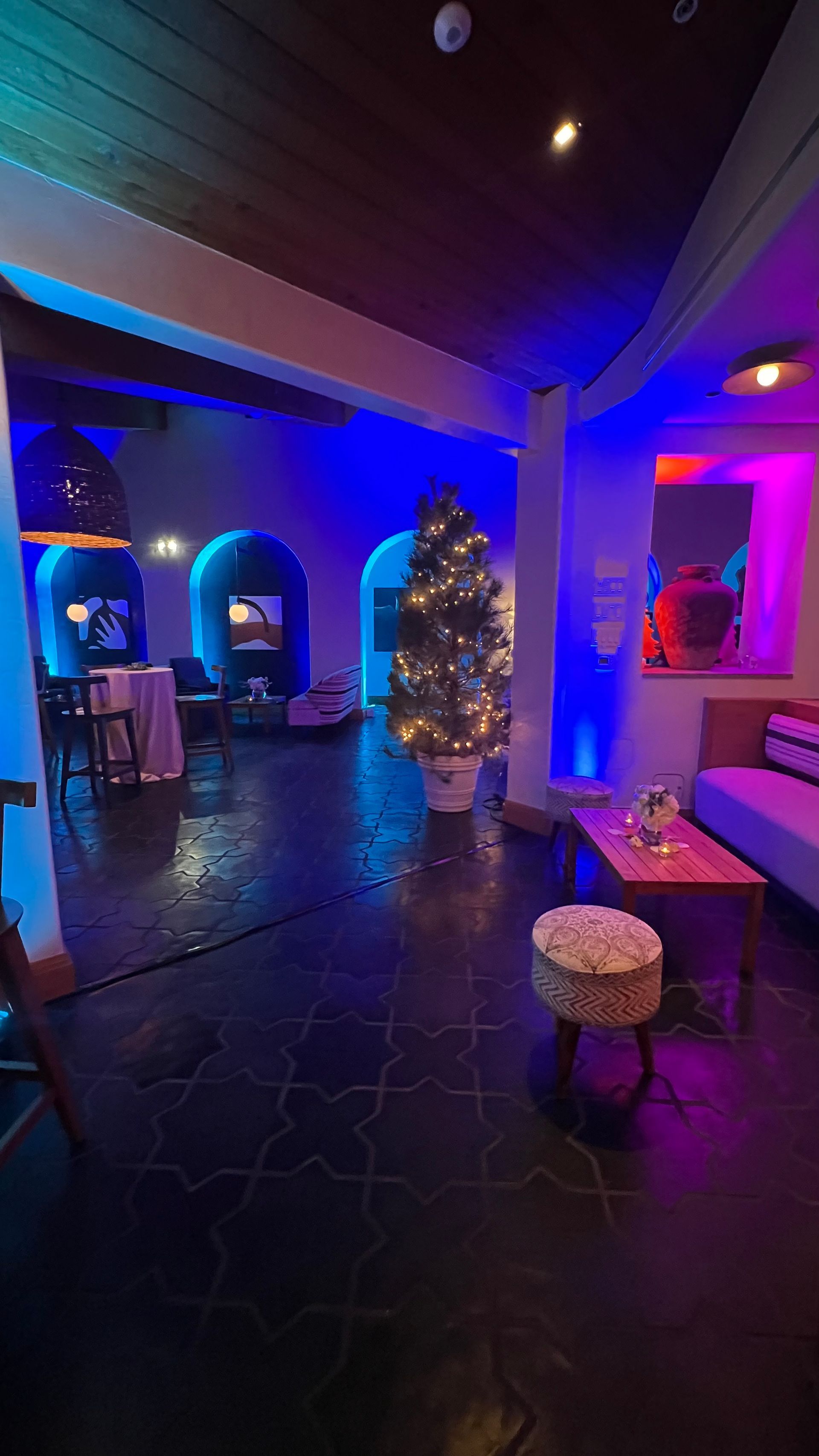 A room with blue and purple lighting, a Christmas tree, and seating areas.